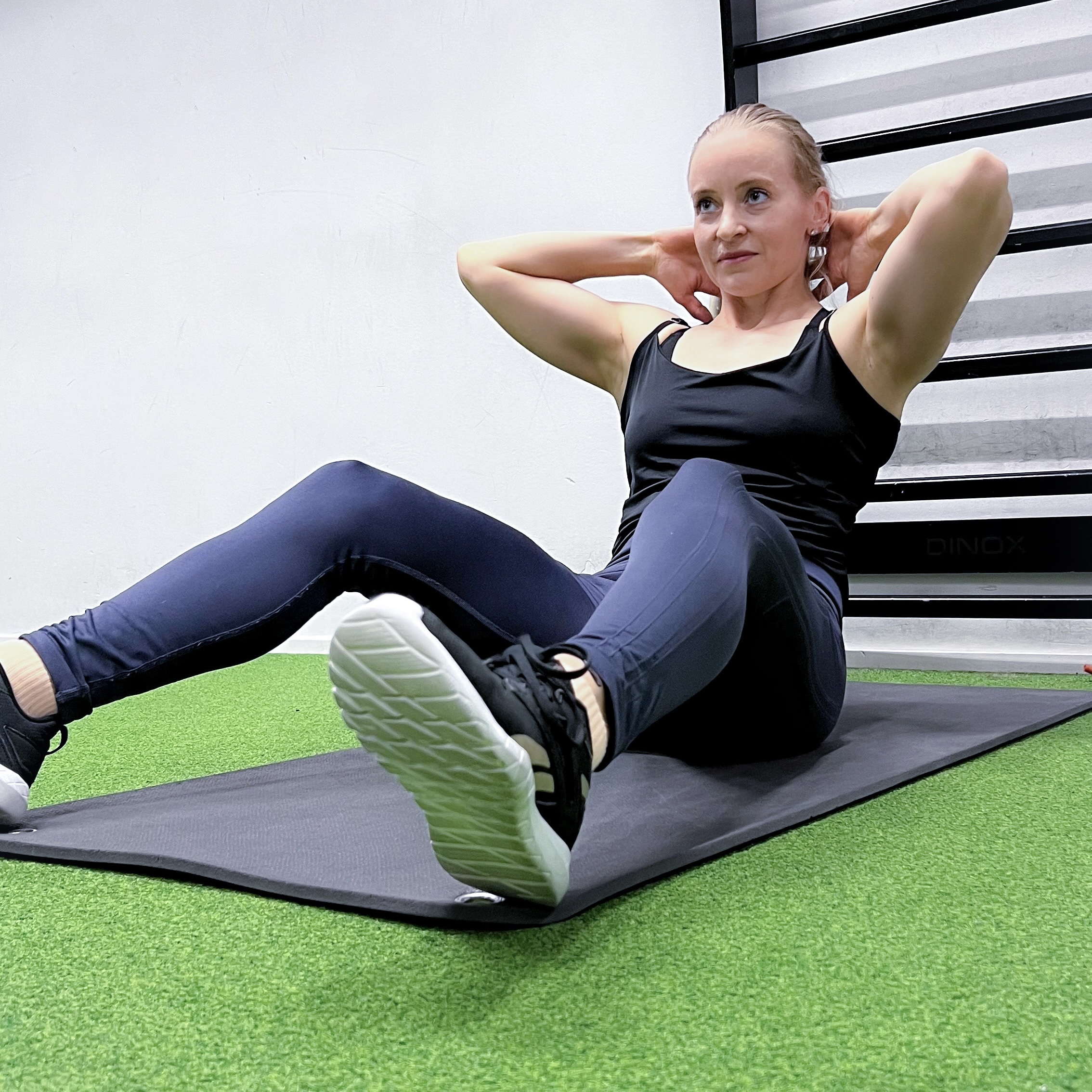 The trainer does a crunch on a mat, hands behind her head